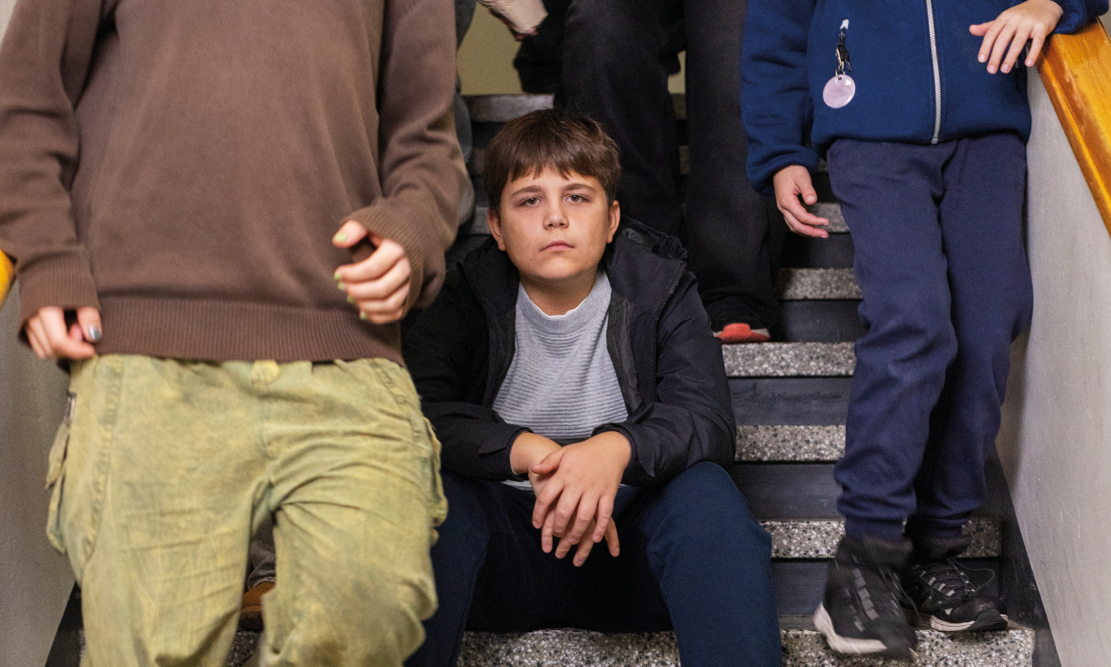 Lapsi istuu koulun portailla ja katsoo kameraan