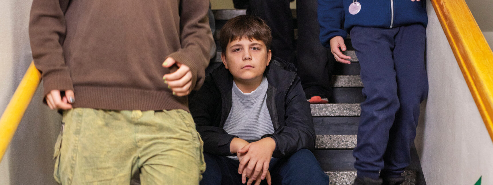 Lapsi istuu koulun portailla ja katsoo kameraan