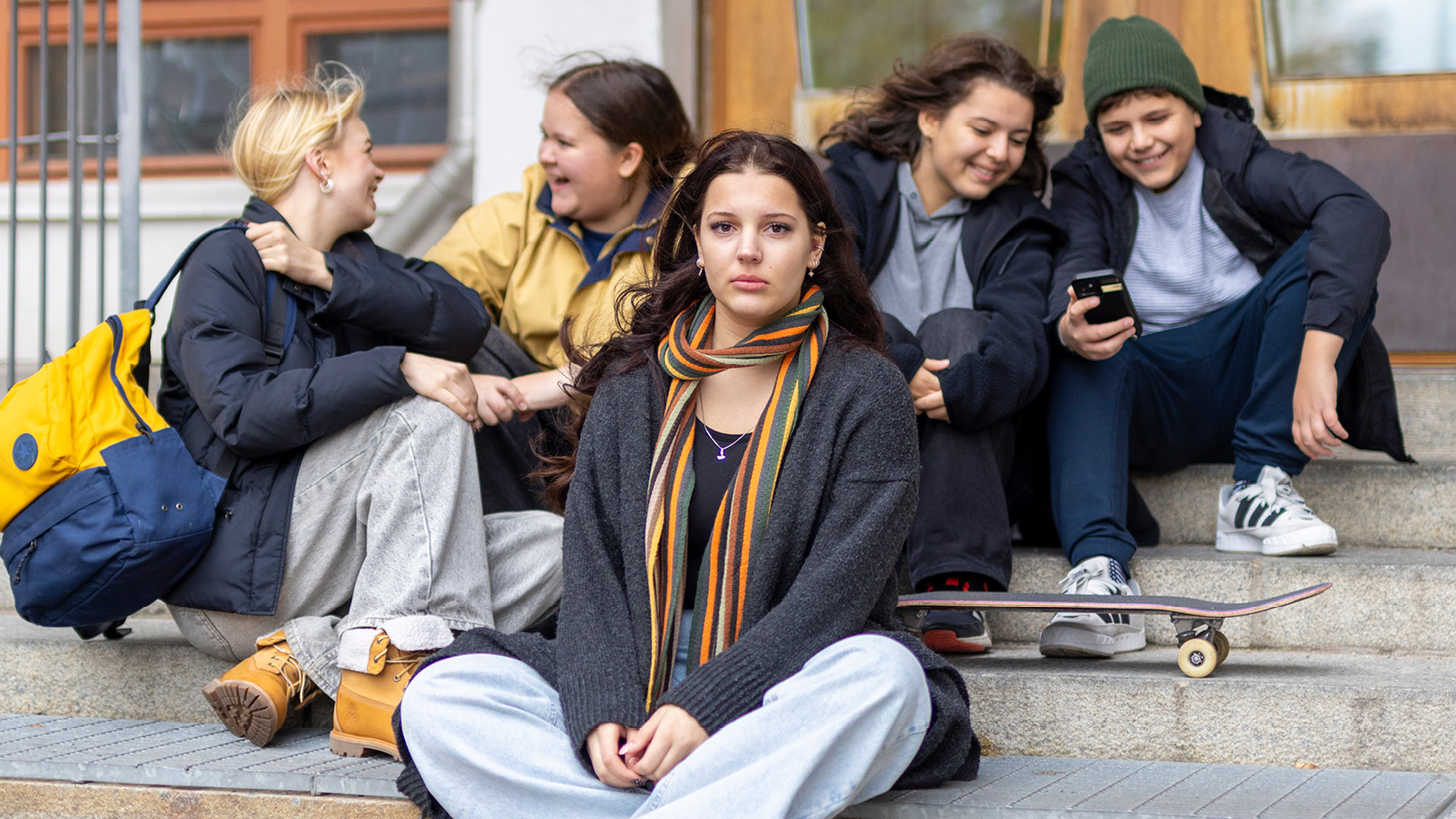 Nuoret istuvat portailla, yksi heistä katsoo vakavana kohti kameraa