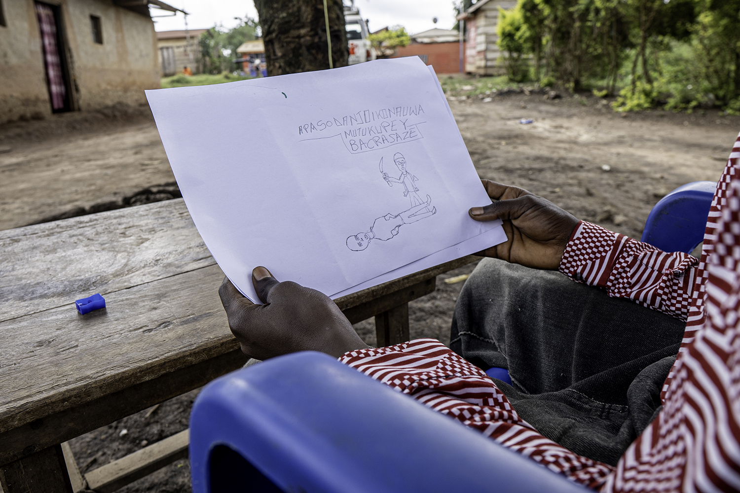 Teini-ikäisen pojan kädet, pitää kädessään pirrustusta, jossa kuva kahdesta hahmosta. Toinen hahmo uhkaa toista väkivallalla.