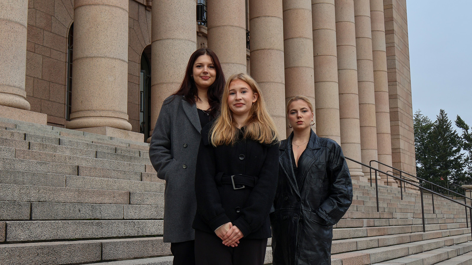 Kolme nuorta seisovat eduskuntatalon portailla.
