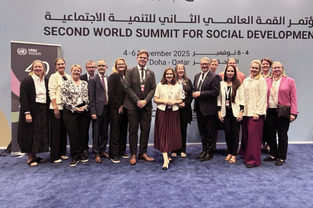 Ryhmä ihmisiä seisomassa seinän edessä, jossa lukee Second World Summit for Social Development