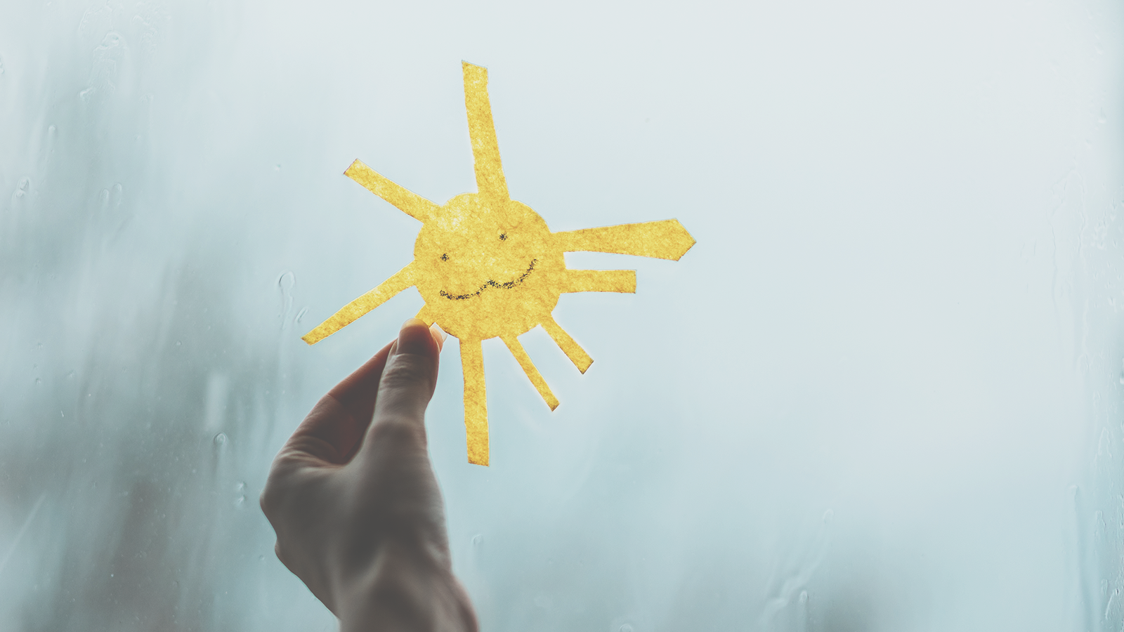 Askarreltu aurinko kädessä harmaan ikkunan edessä