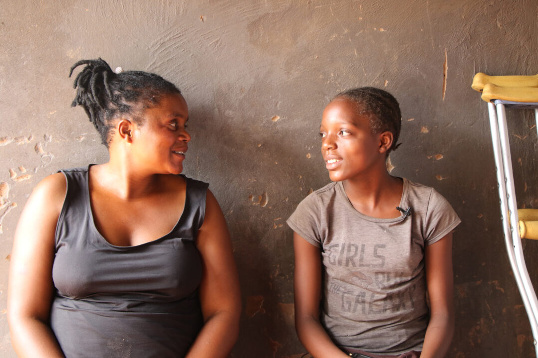 Aikuinen nainen ja teini-ikäinen tyttö istuvat vierekkäin ja katsovat toisiinsa. 