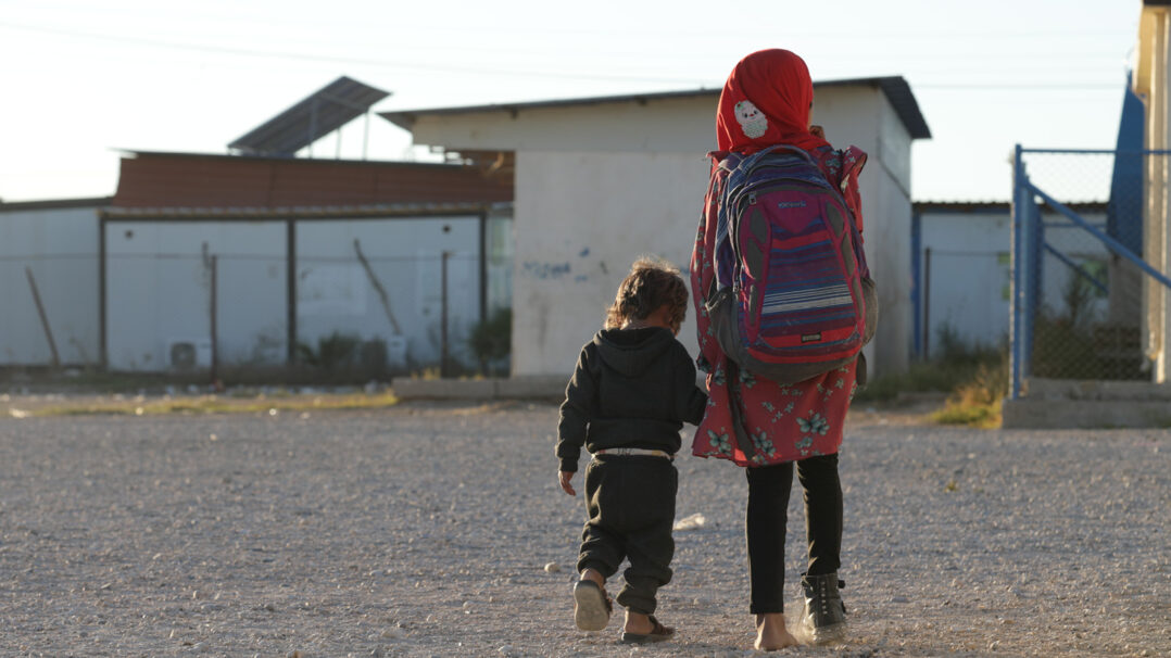 Kaksi lasta kulkevat käsikädessä pakolaisleirillä