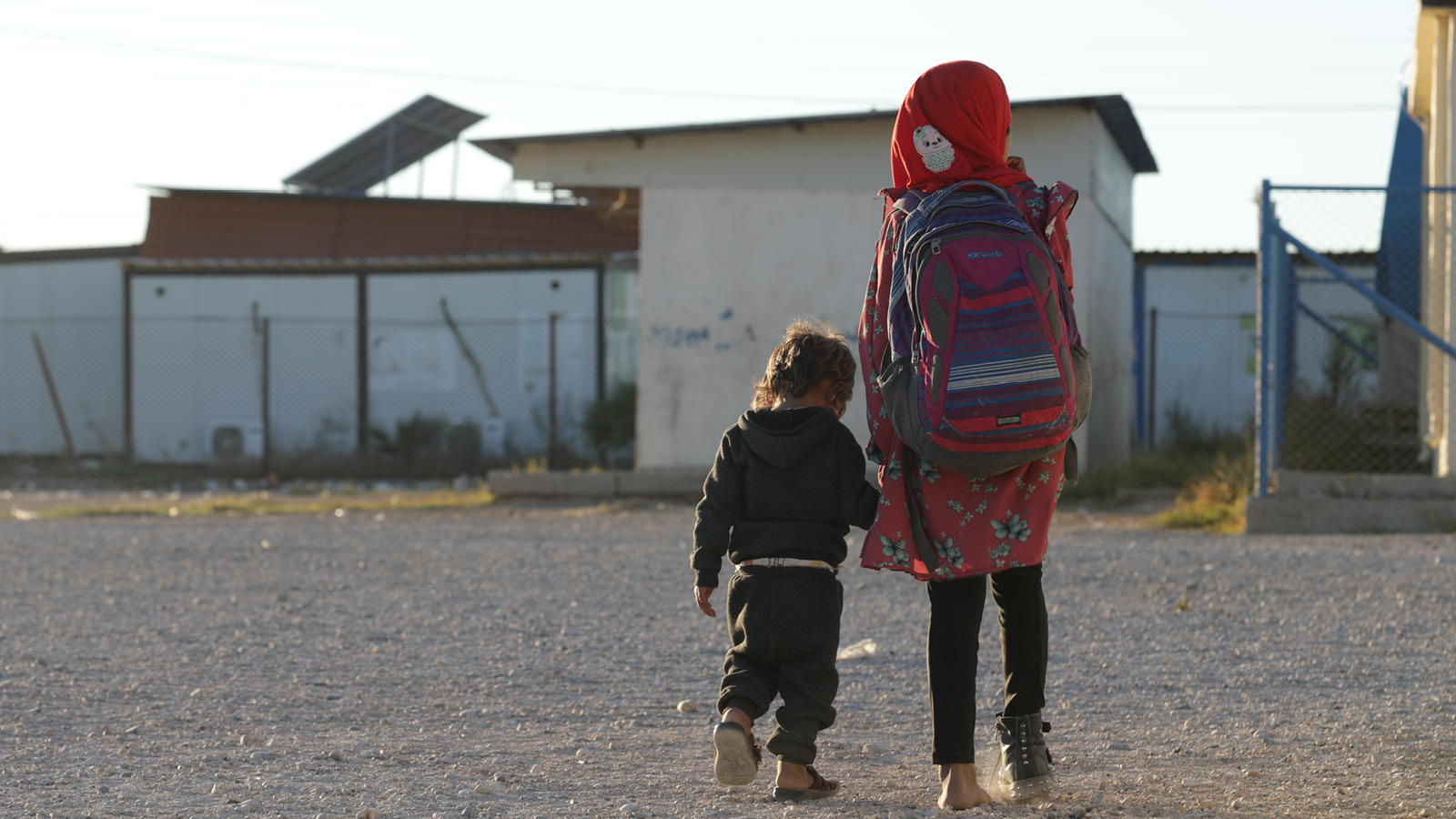 Kaksi lasta kulkevat käsikädessä pakolaisleirillä