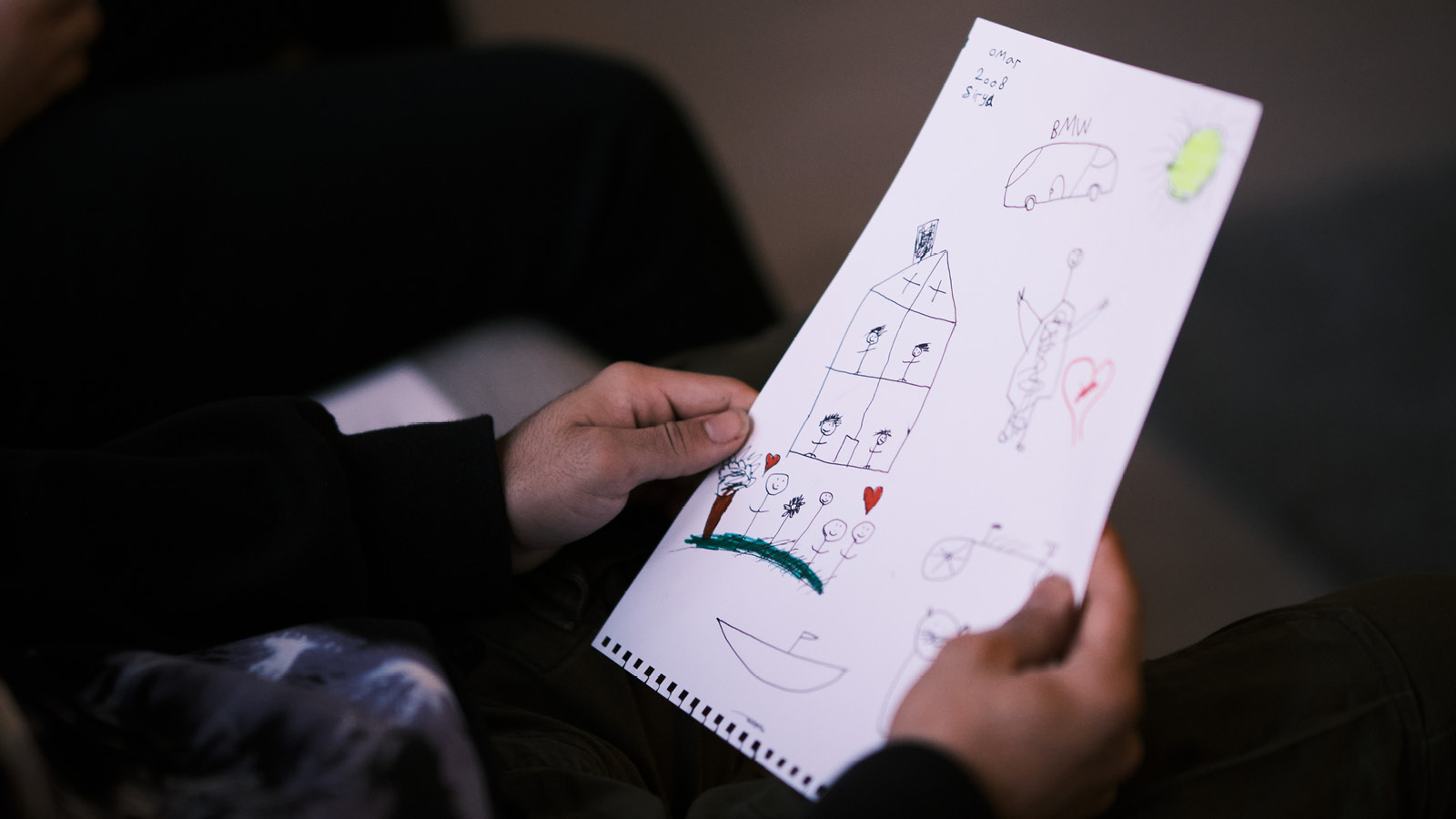 Lapsi pitää käsissään piirrosta, jossa on piirretty värikynillä perhe ja talo.