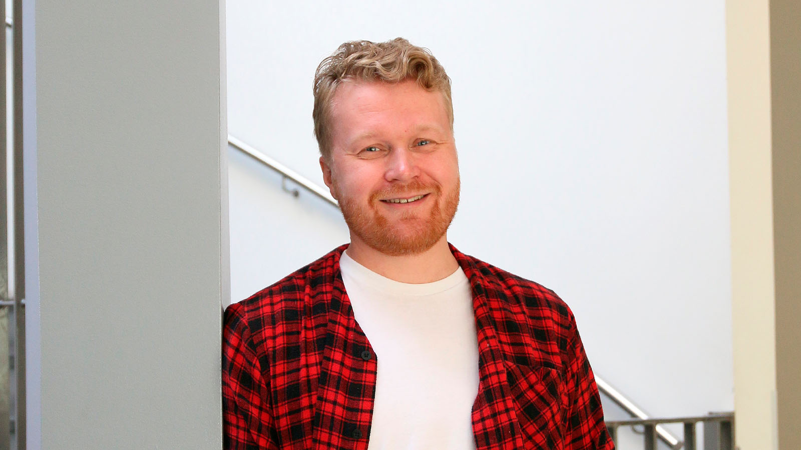 Mies punaisessa paidassa katsoo hymyillen kameraan