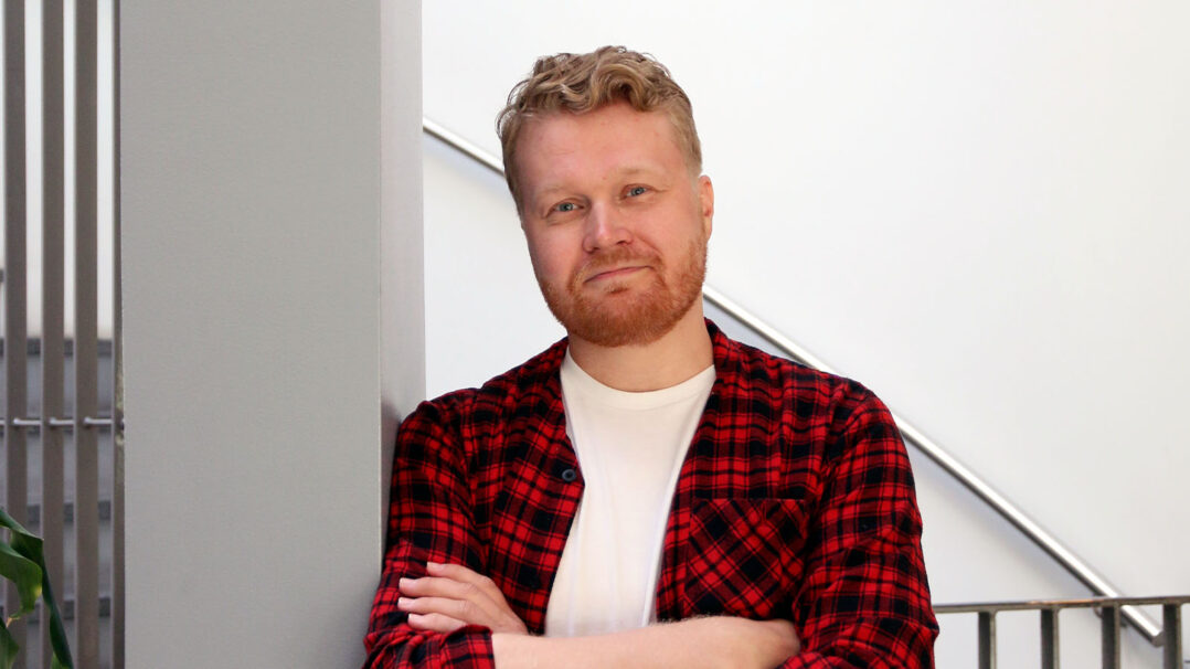 Mies punaisessa paidassa katsoo hymyillen kameraan.