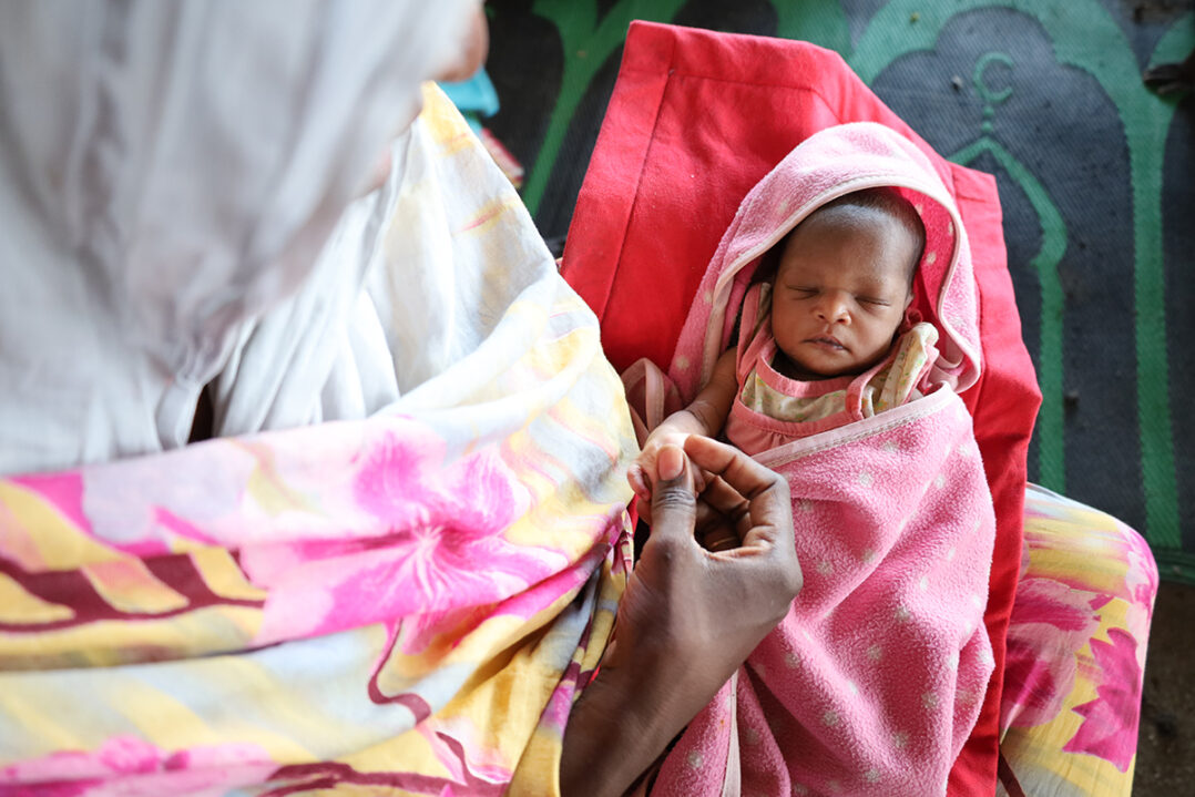 Nainen pitää sylissään vastasyntynyttä vauvaa vilttien välissä. 