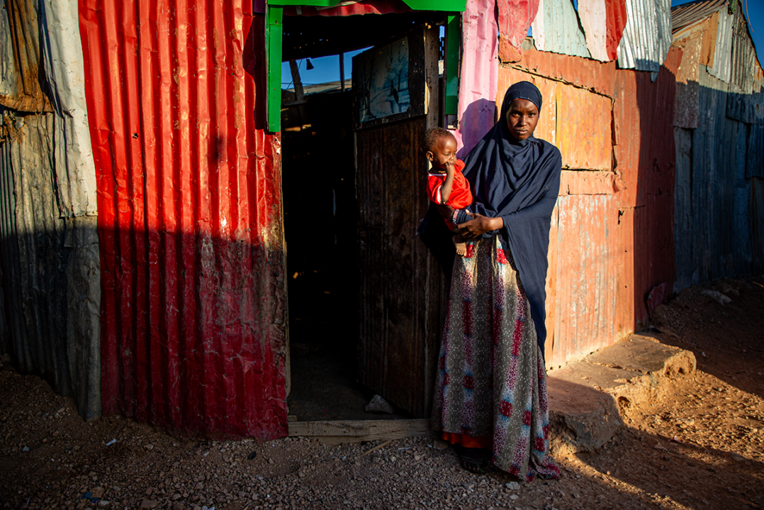 Äiti seisoo vauvansa kanssa peltioven edessä Somaliassa.