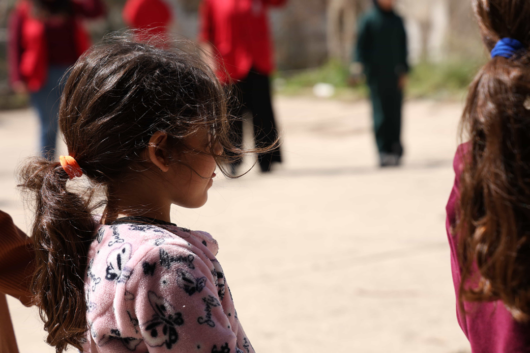 Tyttö seisoo ulkona värikkäässä paidassa ja hänellä on pitkä poninhäntä