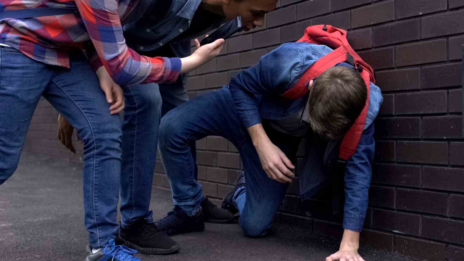 Lapsi ottaa tukea maasta, kiusaajat ovat kumartuneena hänen puoleensa ja kuvaavat puhelimella.