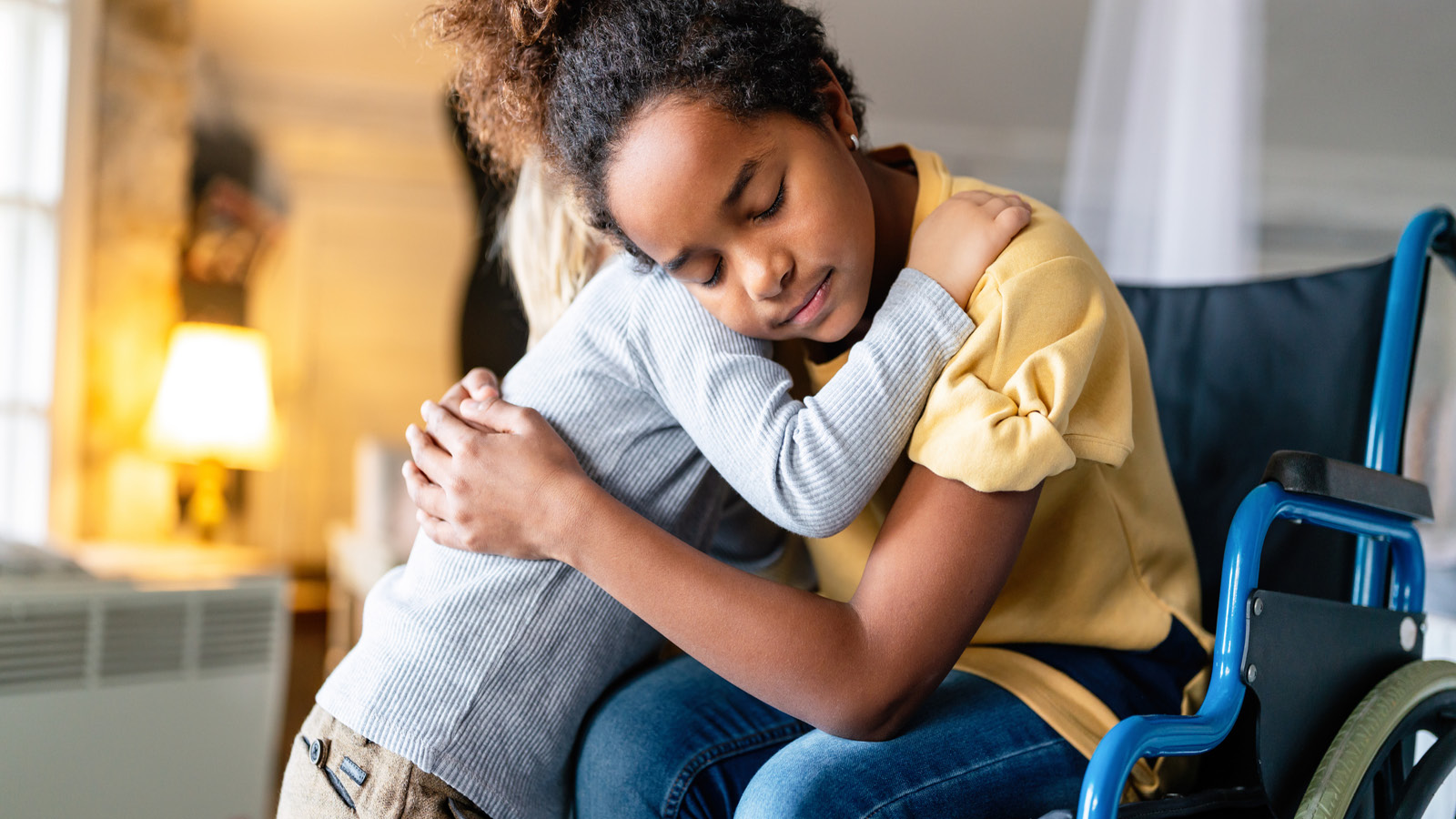 Pyörätuolia käyttävä halaa toista lasta.