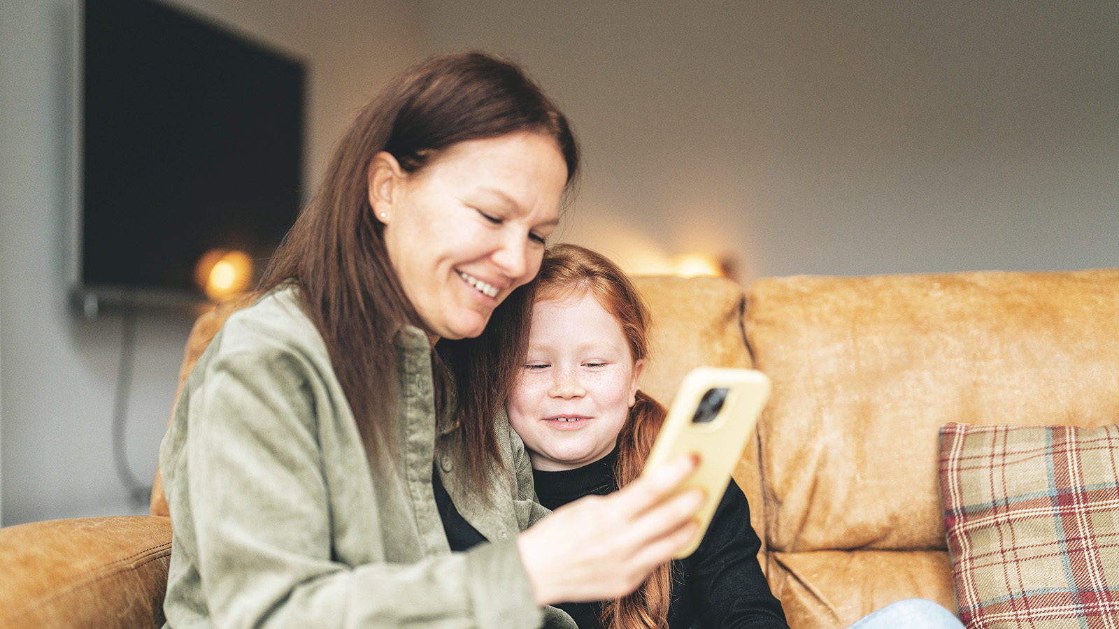 Äiti ja tytär sohvalla yhdessä tutustumassa kännykkään