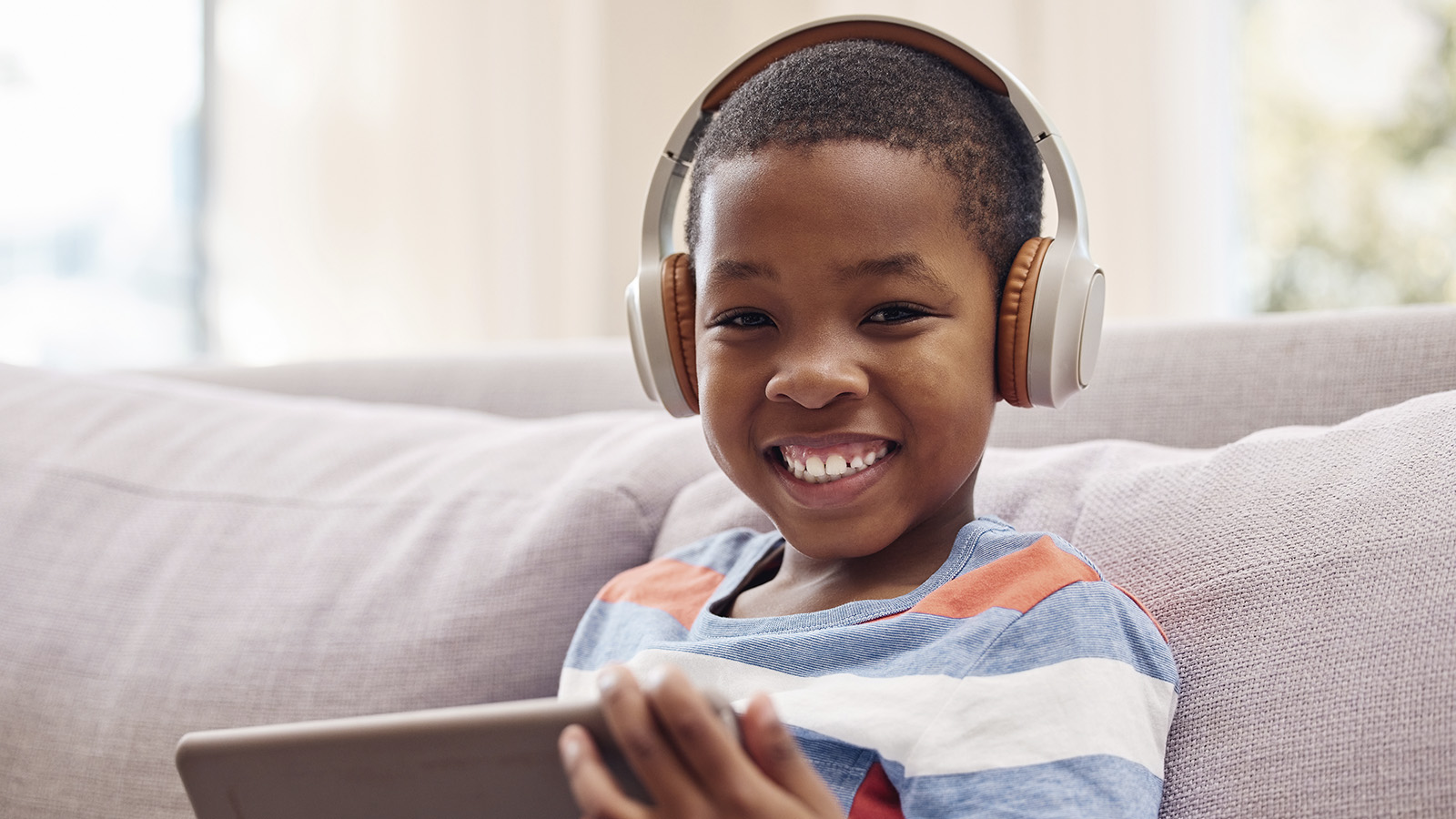 Poika istuu sohvalla kuulokkeet korvailla ja hymyilee