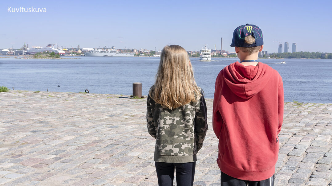 Tyttö ja poika seisovat vierekkäin ja katsovat merelle.