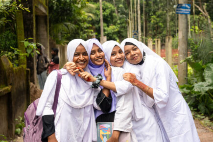 Neljä nuorta seisoo vierekkäin valkoisissa vaatteissa ja hymyilevät. Taustalla vihreää metsää.