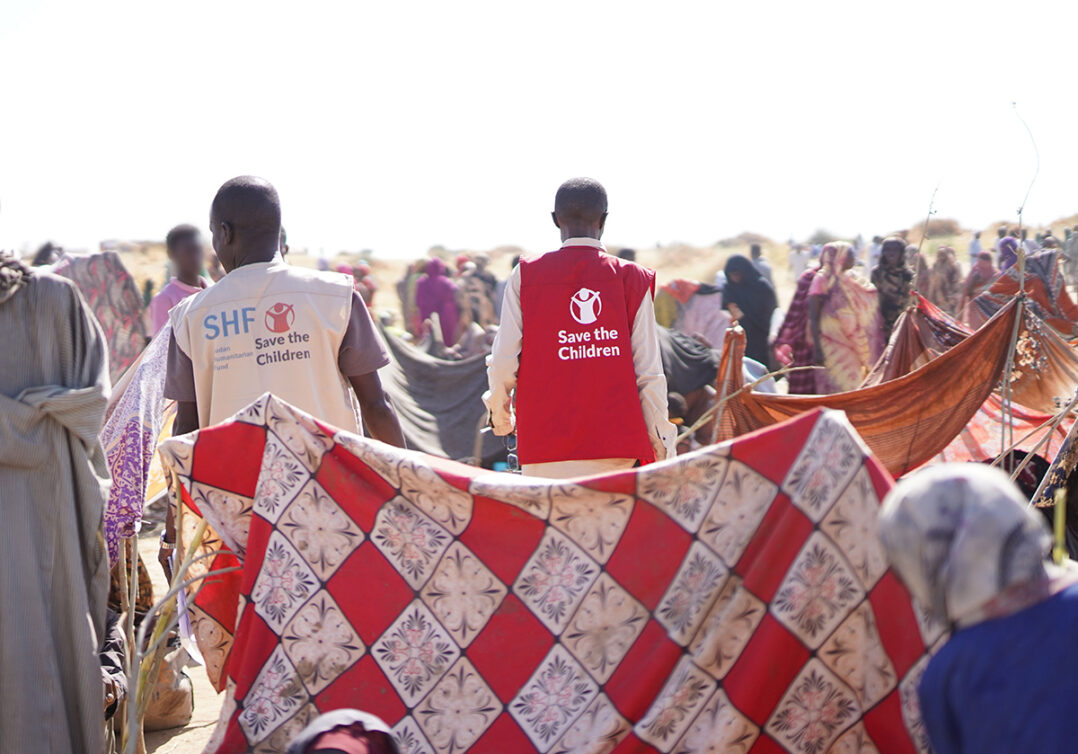 Pelastakaa Lasten työntekijöitä seisoo ihmisjoukossa. Edessä värikäs kangas.