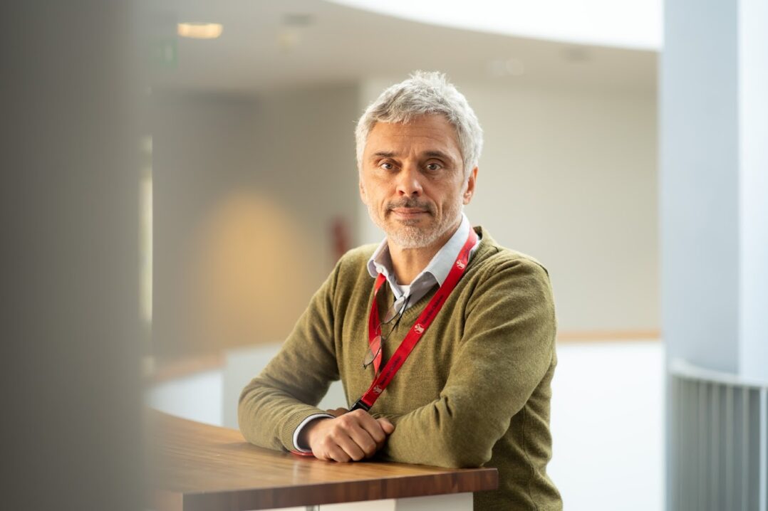 Mies nojaa korkeaan pöytään ja katsoo kameraan.