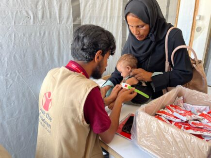 Pelastakaa Lasten työntekijä mittaa lapsen käsivartta. Lapsi on naisen sylissä.
