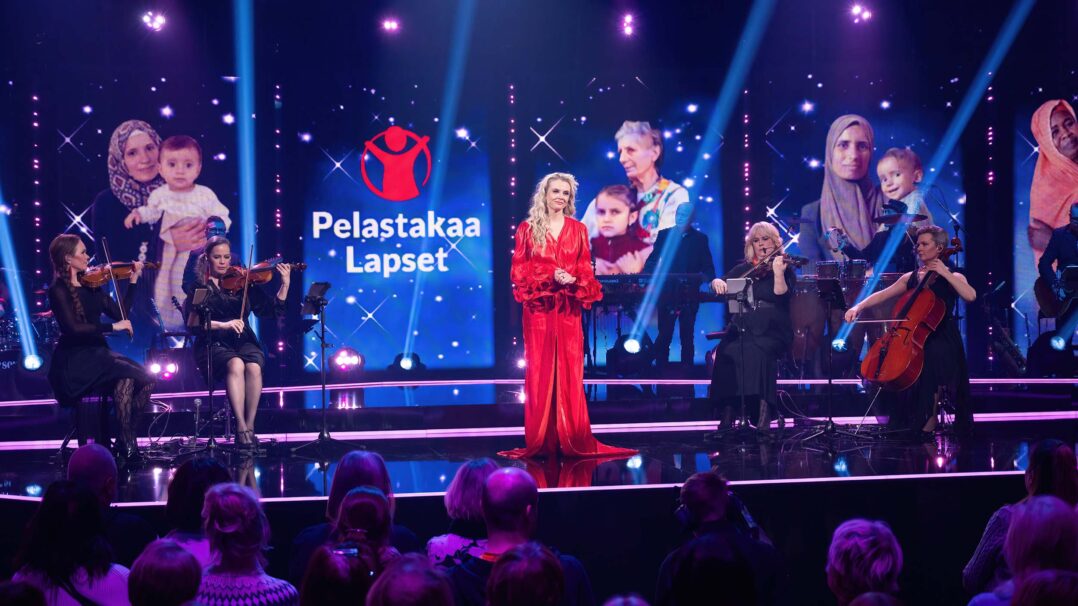 Juontaja Susanna Laine seisoo lavalla punaisessa mekossa.