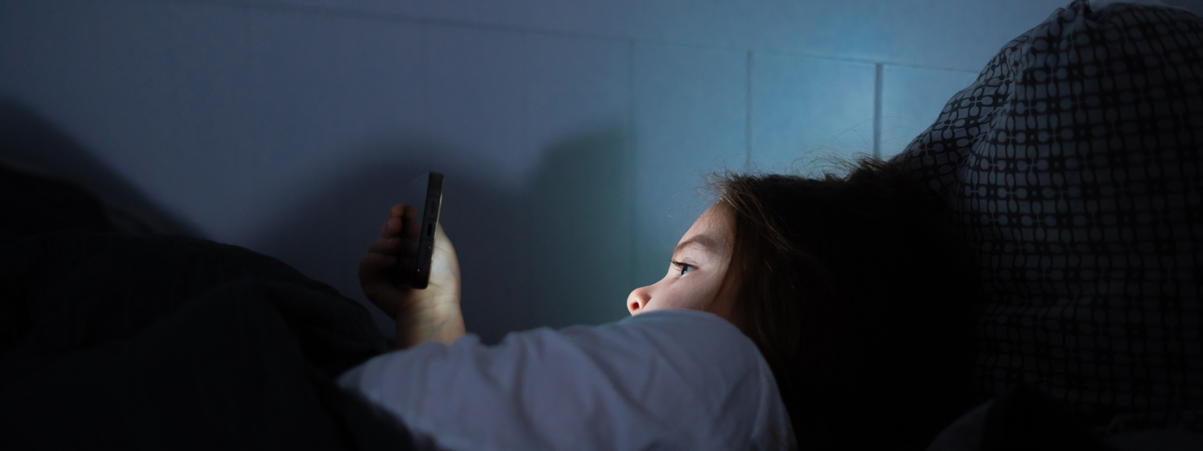 Kuvassa nuori tyttö hämärässä selaamassa puhelinta