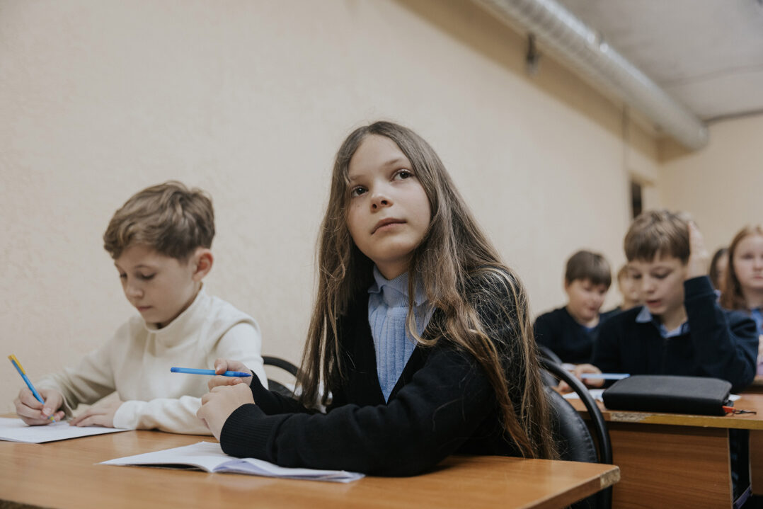 11-vuotias ukrainalainen tyttö istuu pulpetin ääressä ja opiskelee vieressään saman ikäinen poika