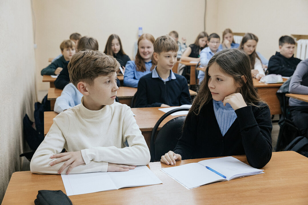 Lapset istuvat luokkahuoneessa. Edessä tyttö ja poika katsovat toisiinsa.