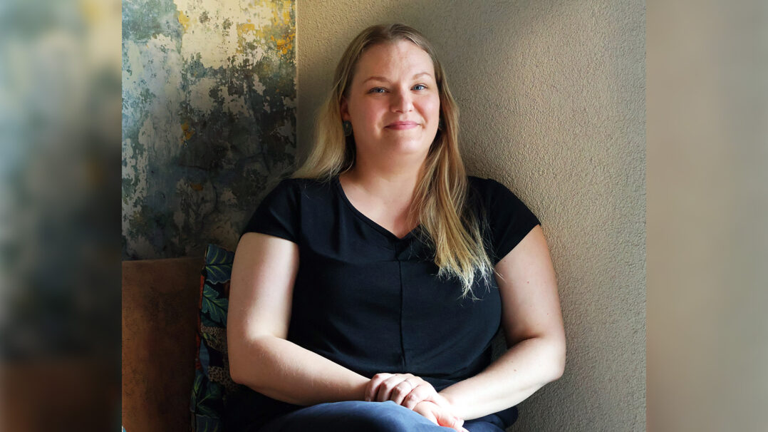 Nainen (Minka) istuu ja hymyilee