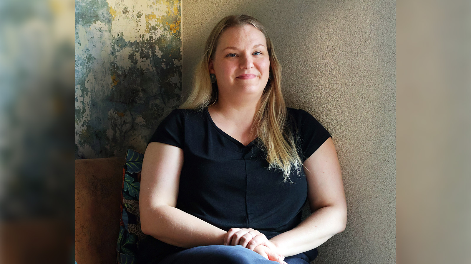 Nainen (Minka) istuu ja hymyilee