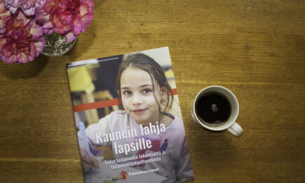 Tilaa testamenttiopas. Kuvassa pöydällä Pelastakaa Lasten testamenttiopas, kahvikuppi ja kukka-asetelma